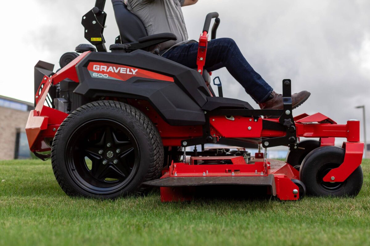 Person operating a red Gravely lawn mower on grass.
