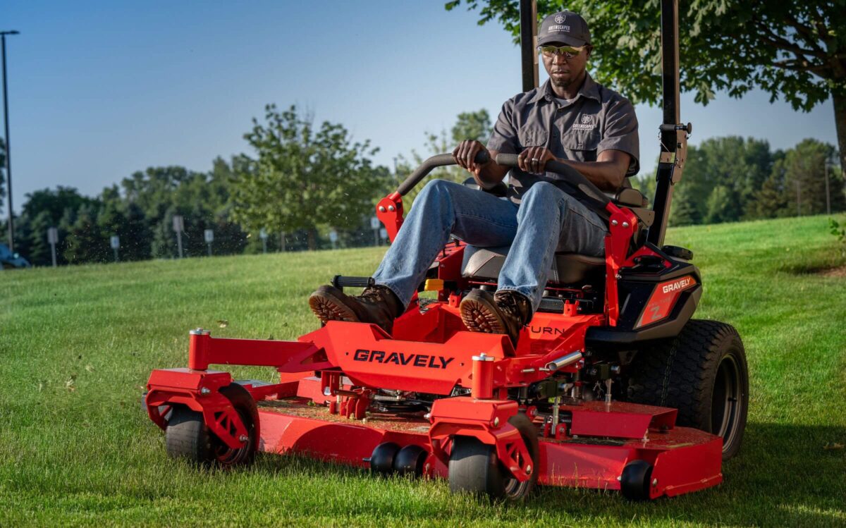 Person mowing grass on a red Gravely zero-turn lawn mower in a park-like setting.