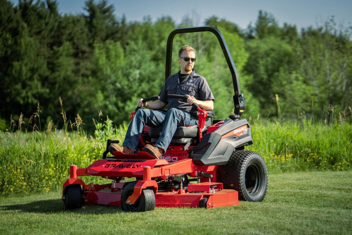 A person operates a red Gravely ZT HD 60 zero-turn lawn mower on a grassy field, with trees in the background.