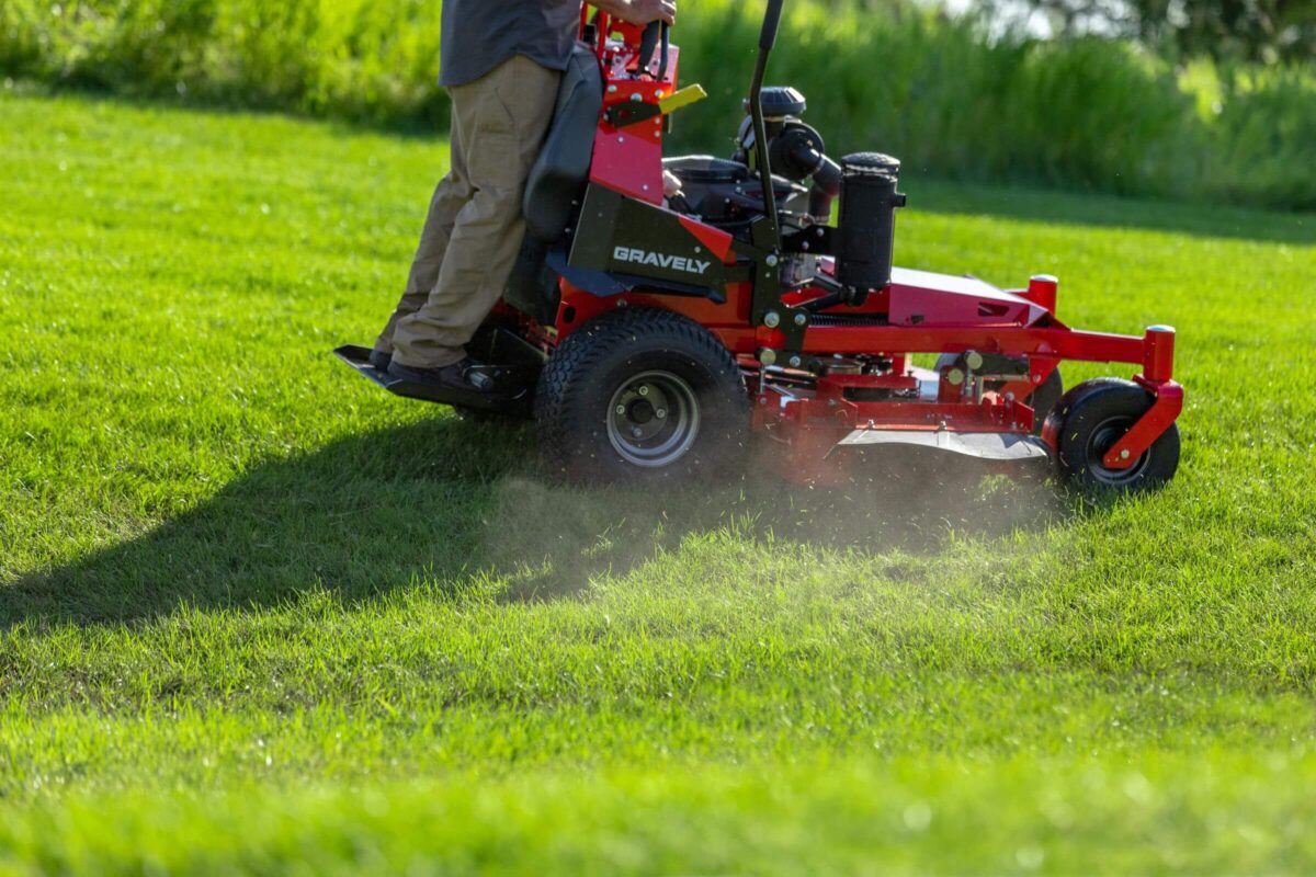 Person operating a red riding lawn mower, cutting grass on a sunny day.