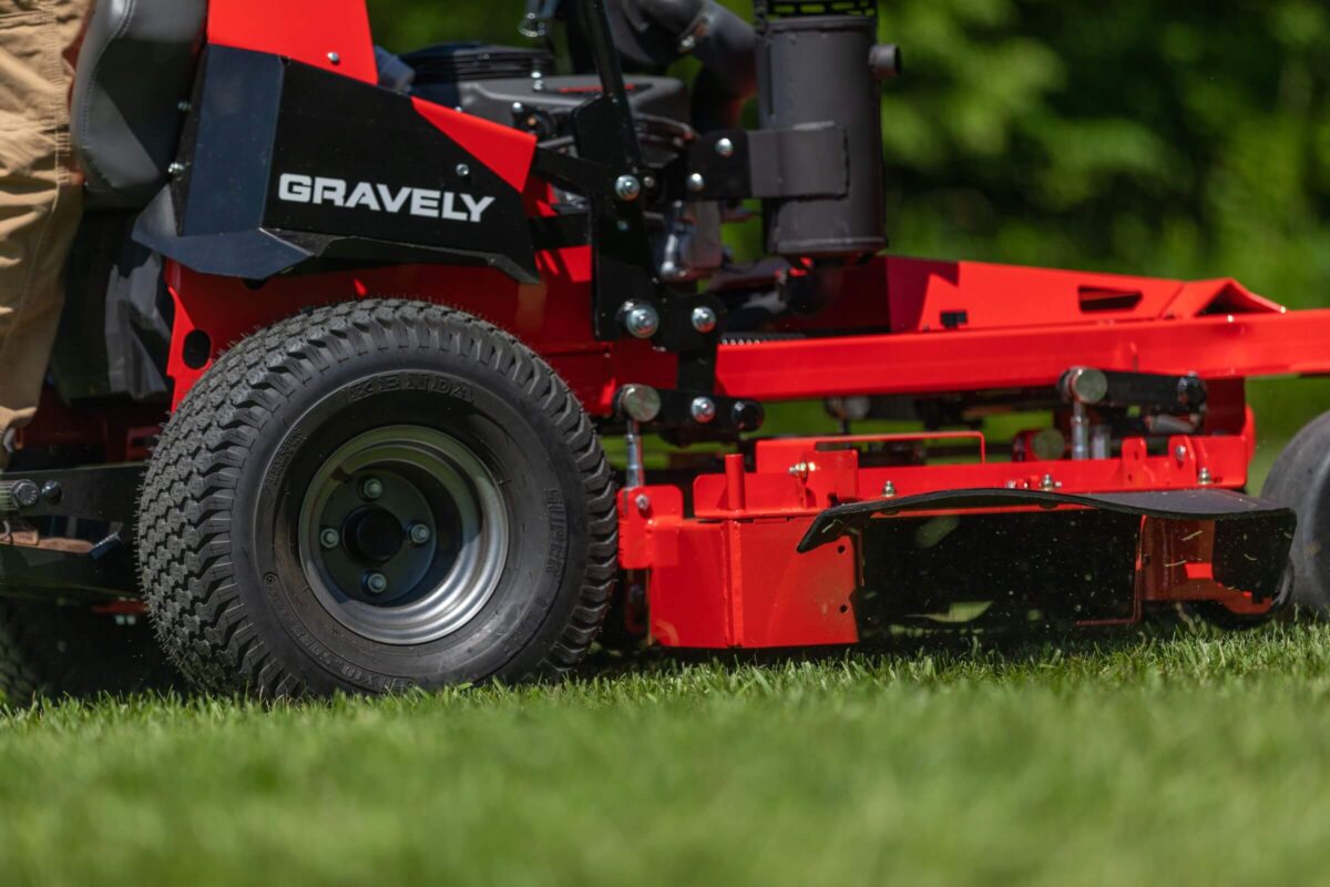 Close-up of a red Gravely lawn mower cutting grass, showing detailed machinery and a large rear tire.