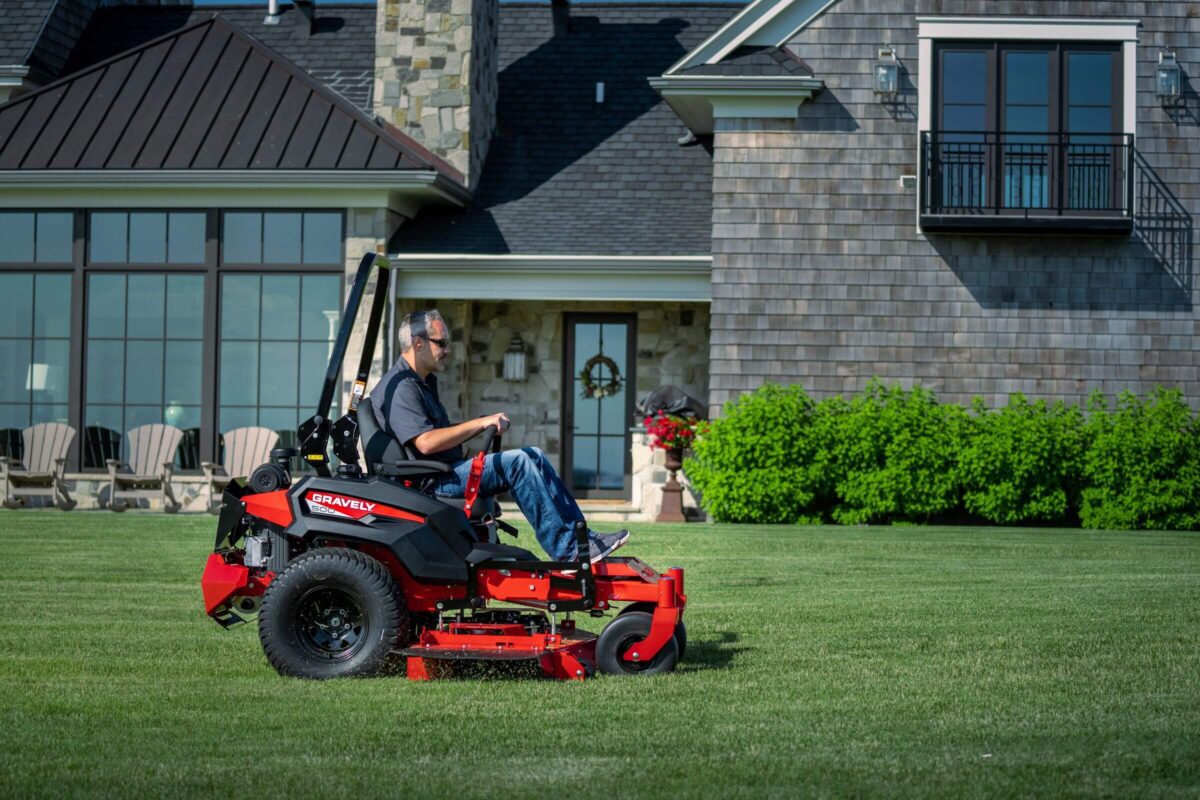 A person is operating a red riding lawn mower on a grassy area in front of a large house.