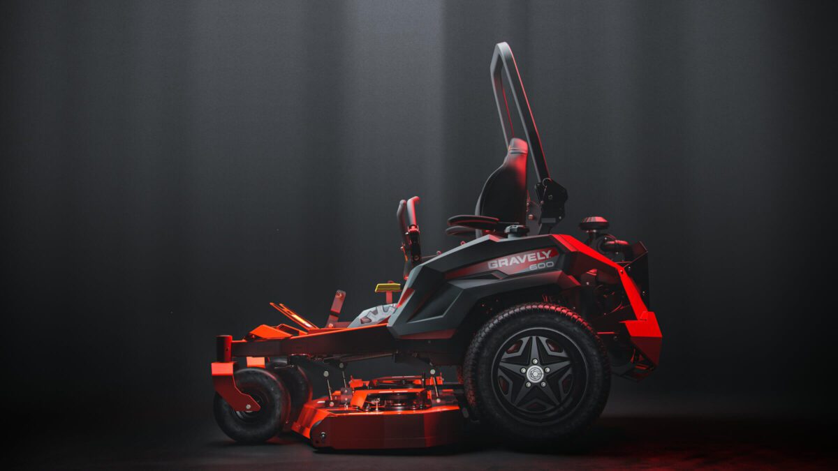 A red and black riding lawn mower with a high-back seat is displayed in a dimly lit setting.