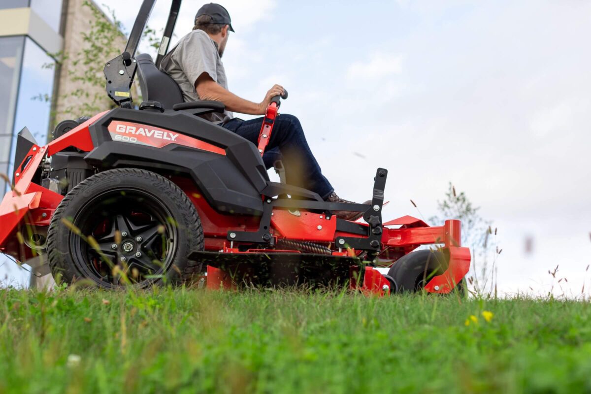 A person operates a red Gravely riding lawn mower on a grassy field.