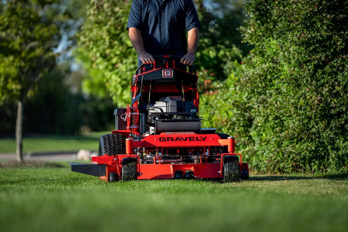 Person operating a red Gravely lawn mower on a grassy area with trees in the background.