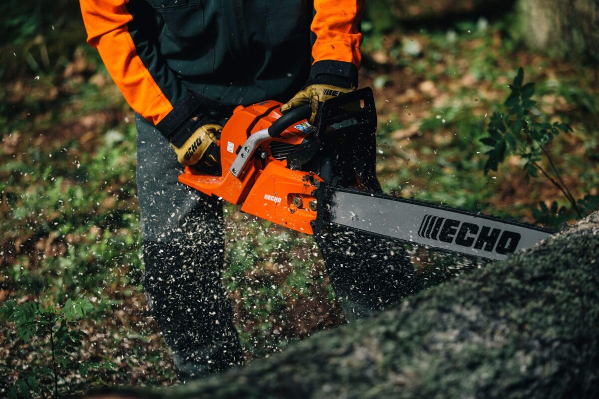 Person in protective gear using a CS-620SX-1750 chainsaw to cut a fallen tree outdoors.