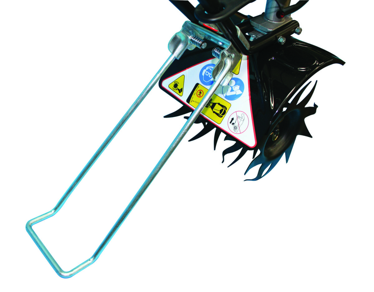 Close-up of a garden tiller's metal tines and handles. The triangular panel displays various warning stickers.
