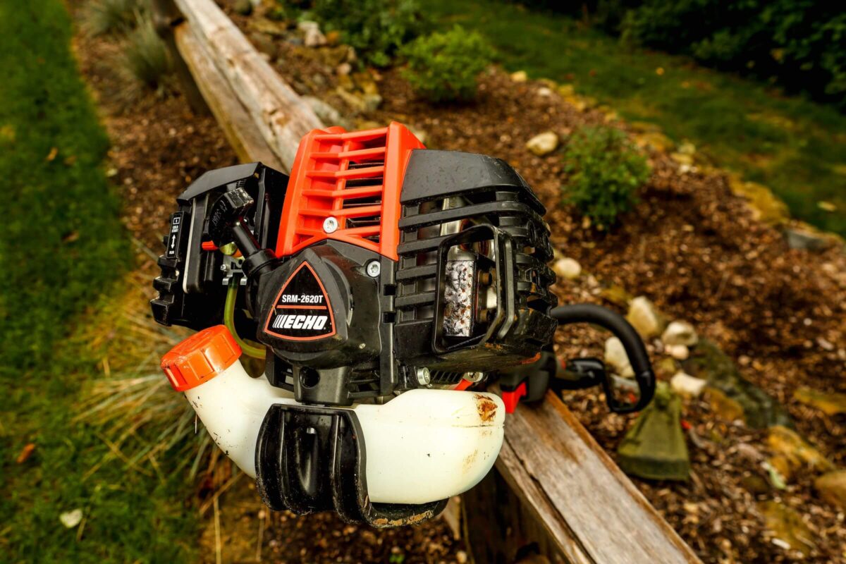 Gas-powered leaf blower resting on a wooden railing in a garden setting.